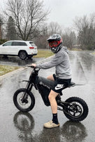 Joven con casco sentado sobre una moto eléctrica Soleil01 SE negra en una carretera mojada durante un día lluvioso
